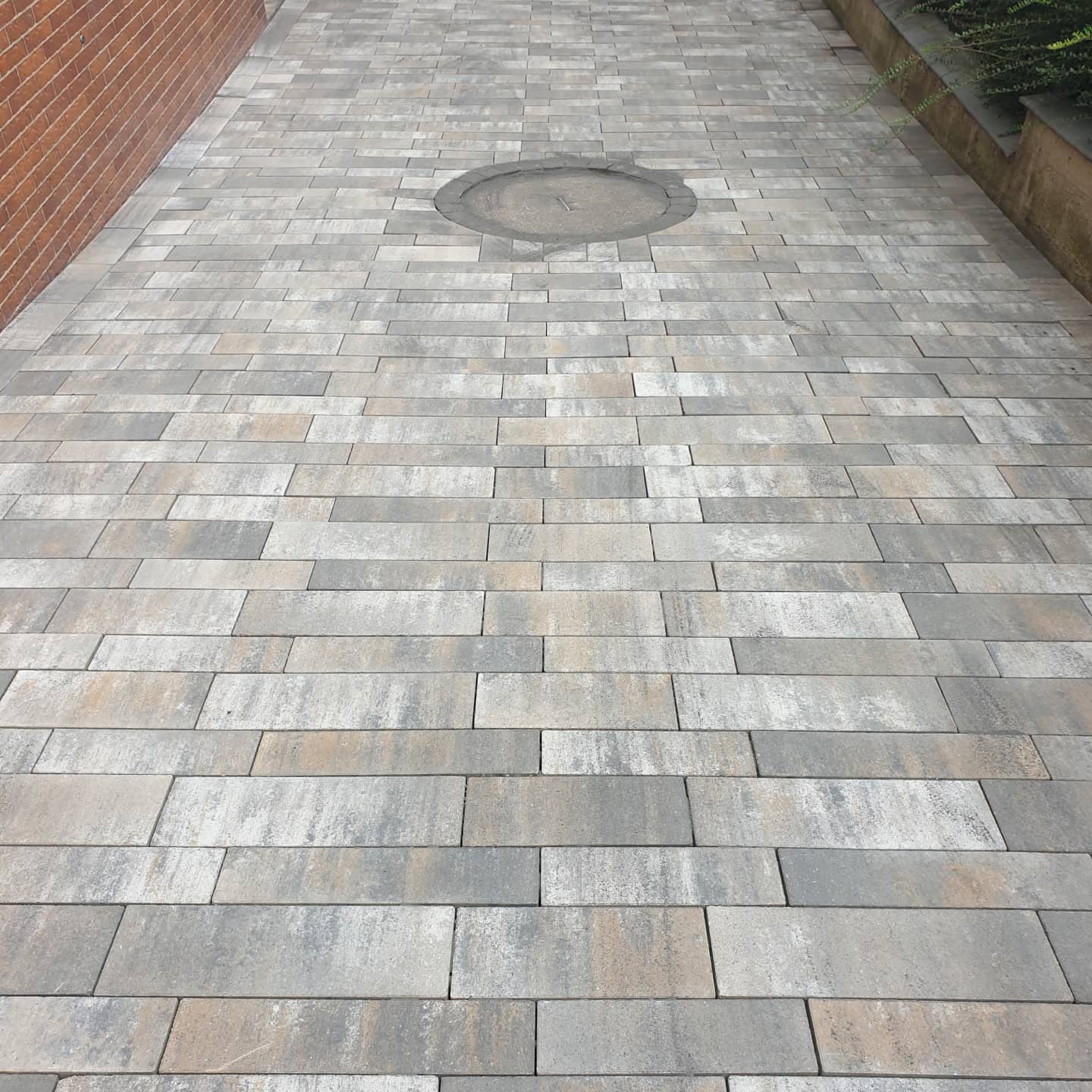 Gehweg aus grauem Pflaster mit Schachtdeckel